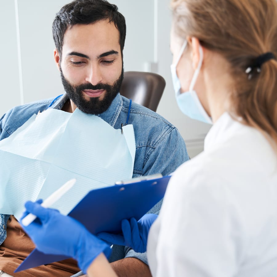 A dentist and a patient review the patient's oral health. A screen shows a digital rendering of her upper teeth.